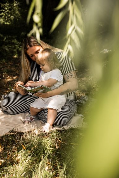 Intimes Mutter-Kind-Shooting in Kassel - durch Blätter fotografiert beim gemeinsamen Buchlesen im warmen Licht.