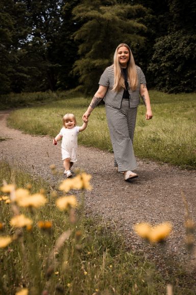Wilde Hummelfotografie in Kassel -Fröhliches Mommy und Me Shooting  auf einem Naturweg mit Blüten im Vordergrund.